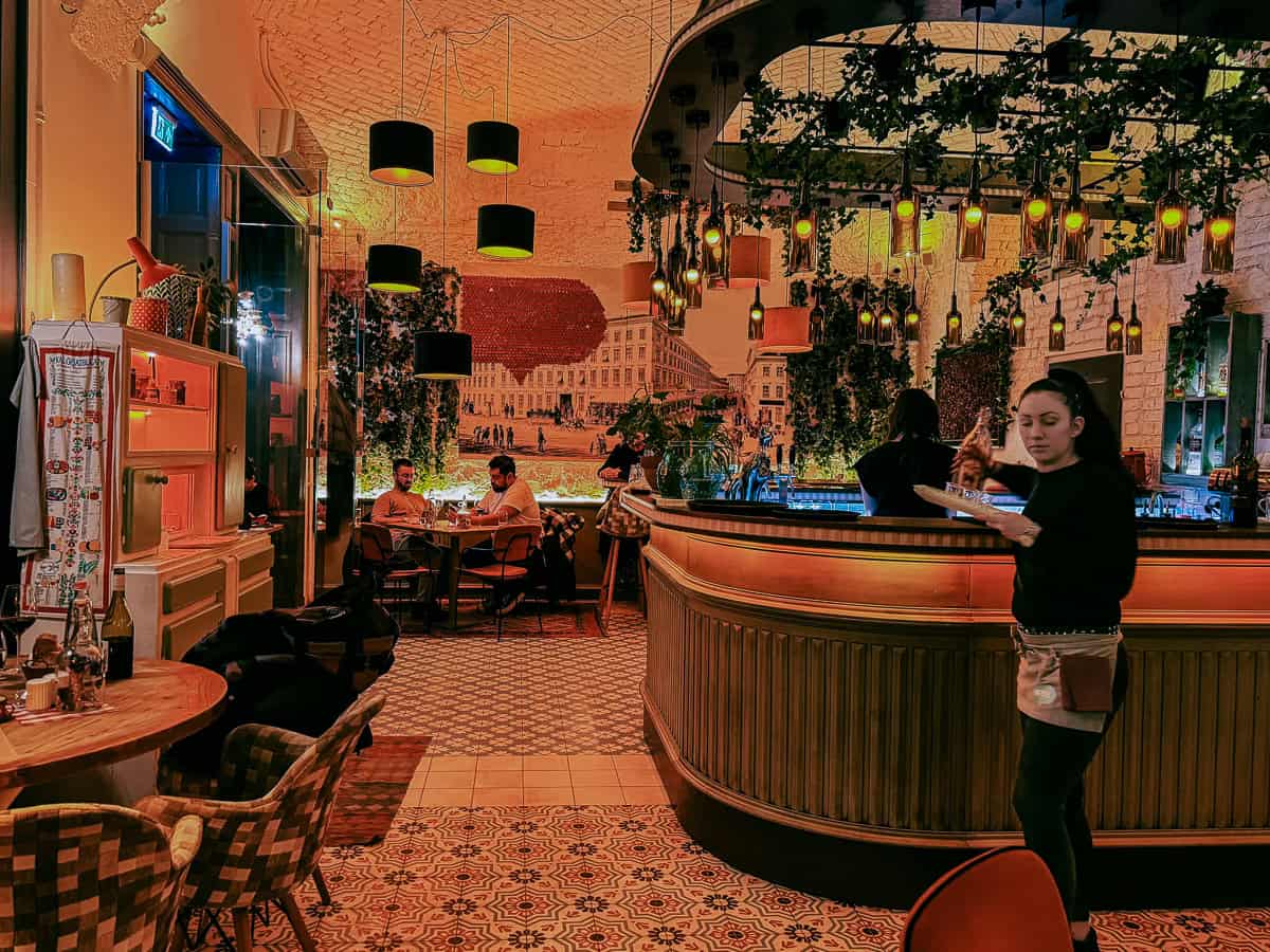 The interior of a vibrant restaurant with a curved bar, hanging lights, and diners enjoying their meals in a warmly lit environment.