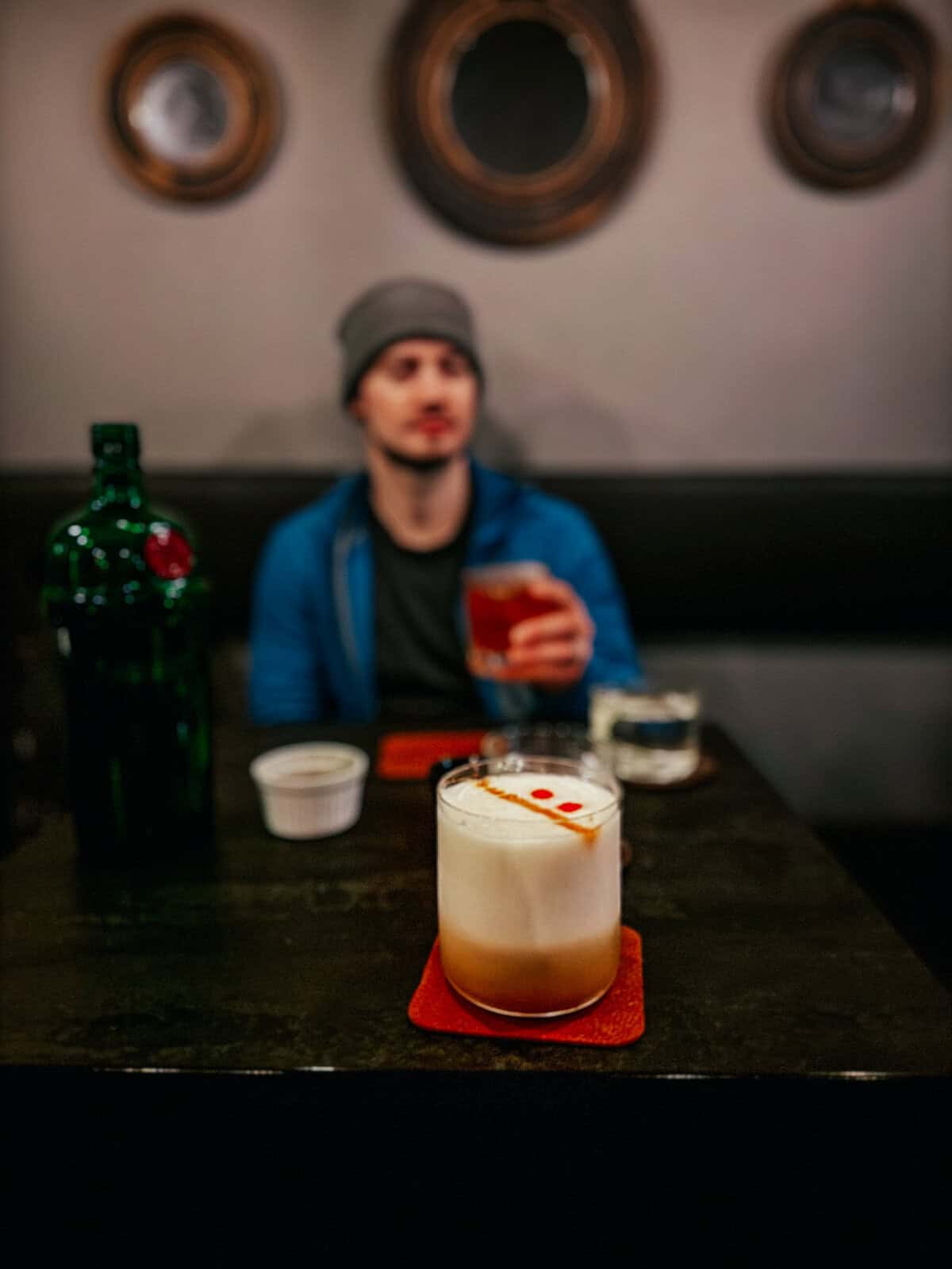 my husband in a blue beanie holding a drink with a frothy cocktail on a table in front of me