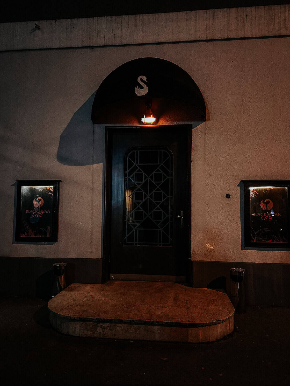 The exterior of 'Black Swan' bar, featuring a single door with a small light above it and posters on either side.