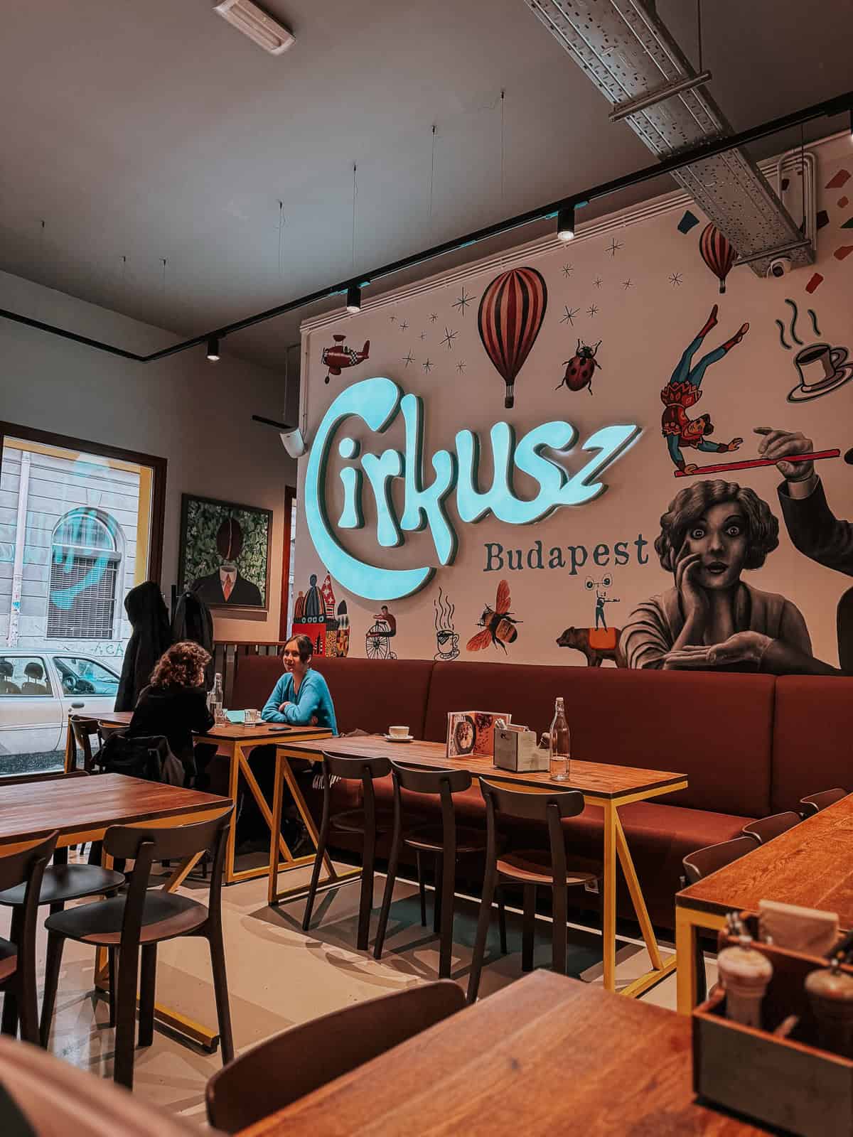 Interior of Cirkusz café in Budapest, featuring a colorful wall mural with the café’s name and illustrations of hot air balloons and circus performers.