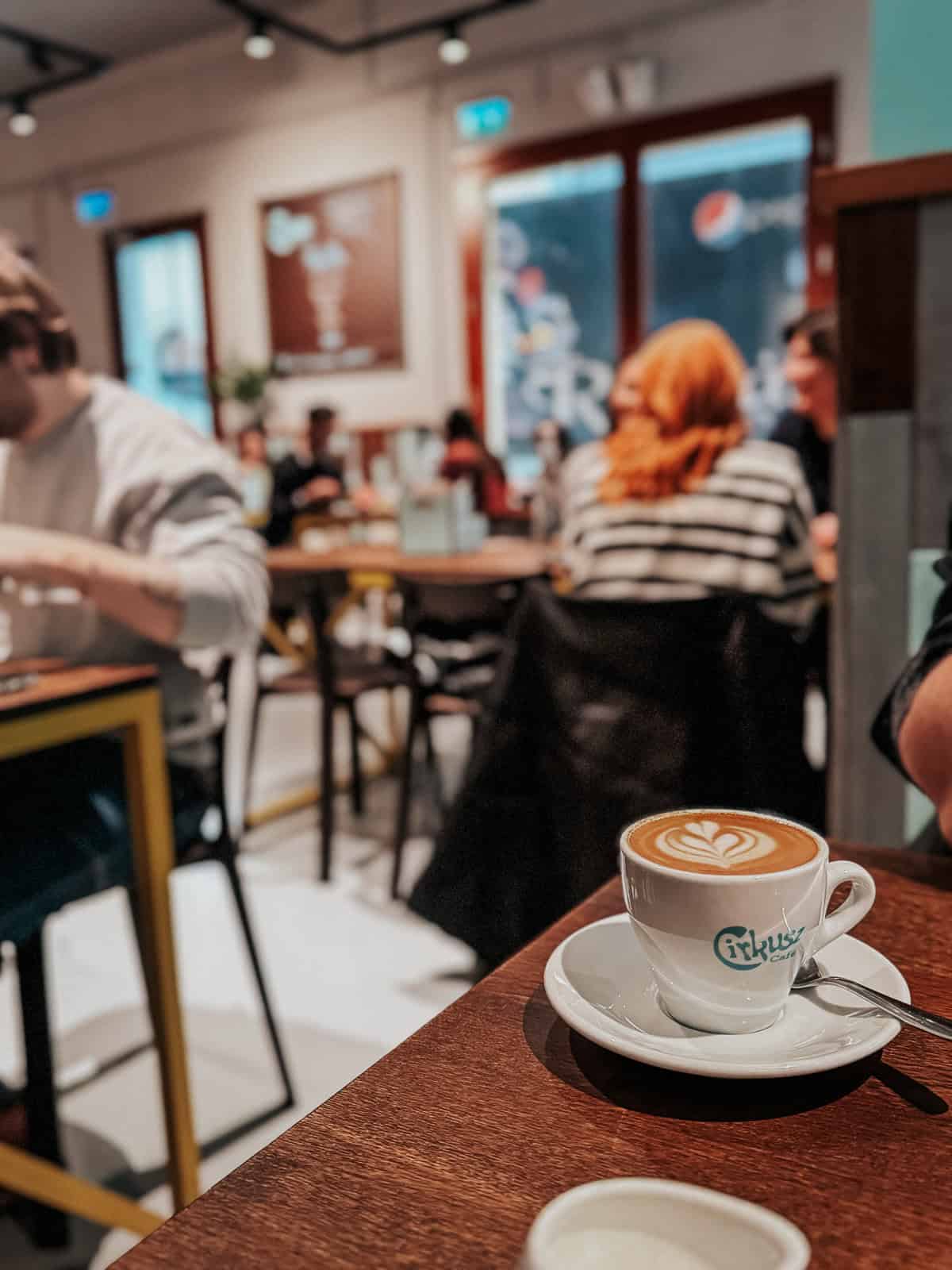 Close-up of a cup of coffee on a table in Cirkusz café, with people dining in the background.