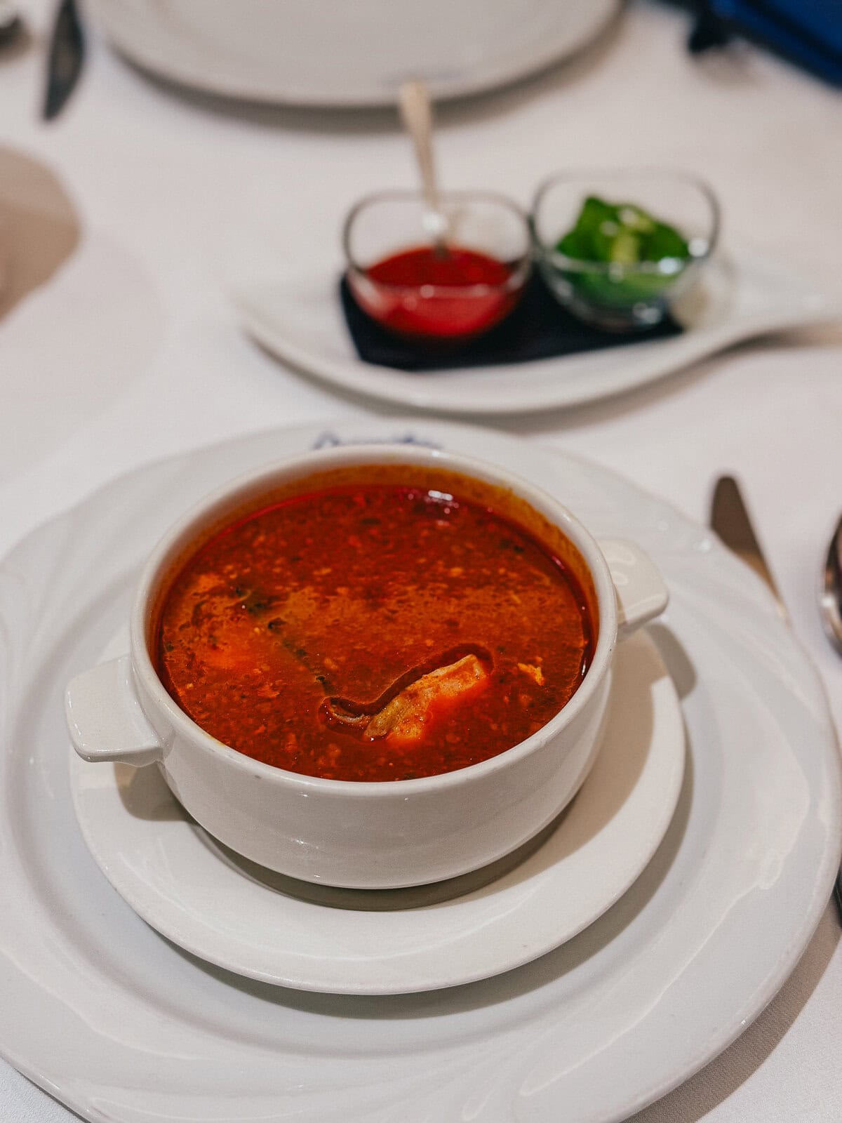 A bowl of Hungarian fisherman's soup (halászlé) with a rich red broth, served with condiments on the side.