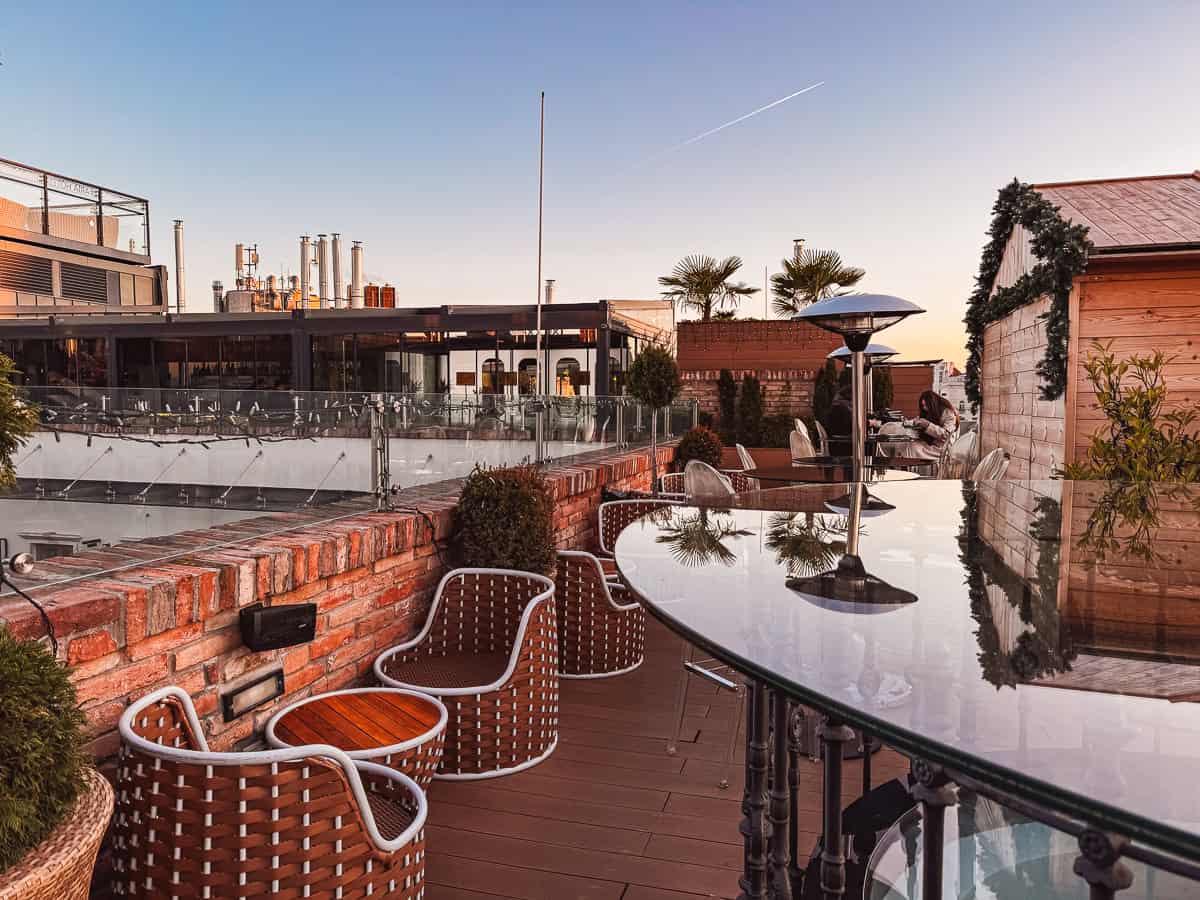 A cozy rooftop bar with modern seating, glass tables, and warm lighting, capturing the ambiance of a sunset.