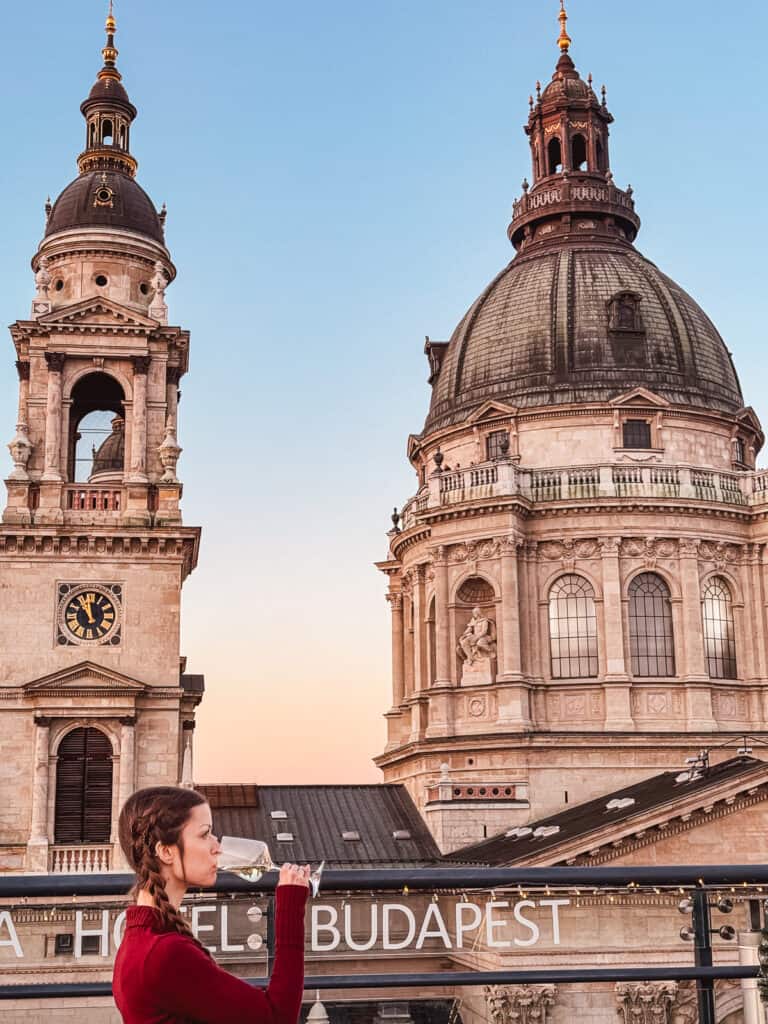 A woman sipping champagne on a rooftop terrace with a stunning view of St. Stephen's Basilica in the background at sunset