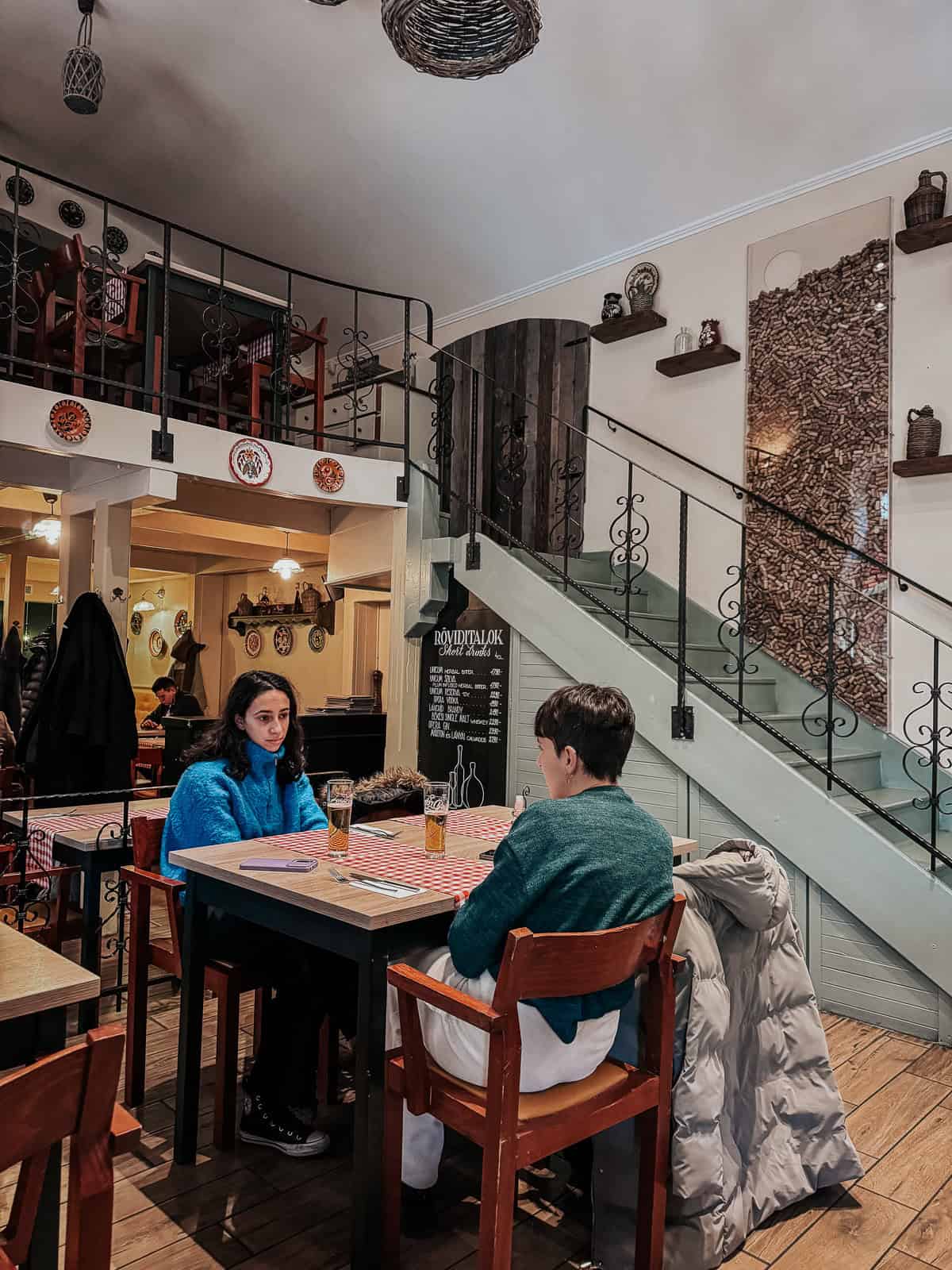 A cozy restaurant setting with a mezzanine floor, decorative plates on the walls, and diners enjoying their meals at wooden tables.