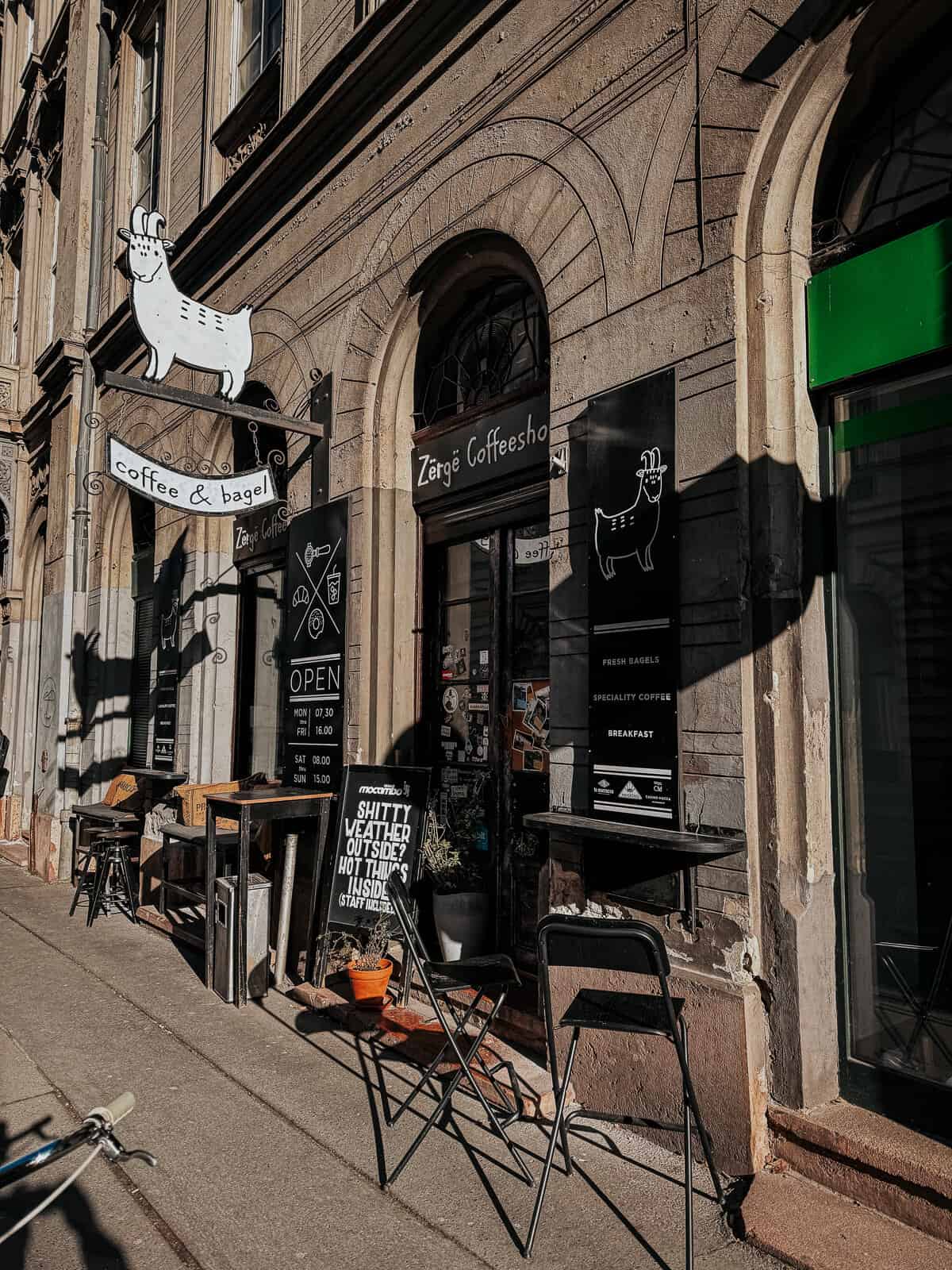 The exterior of Zérge Coffeeshop, featuring outdoor seating and a sign with a cartoon goat logo.