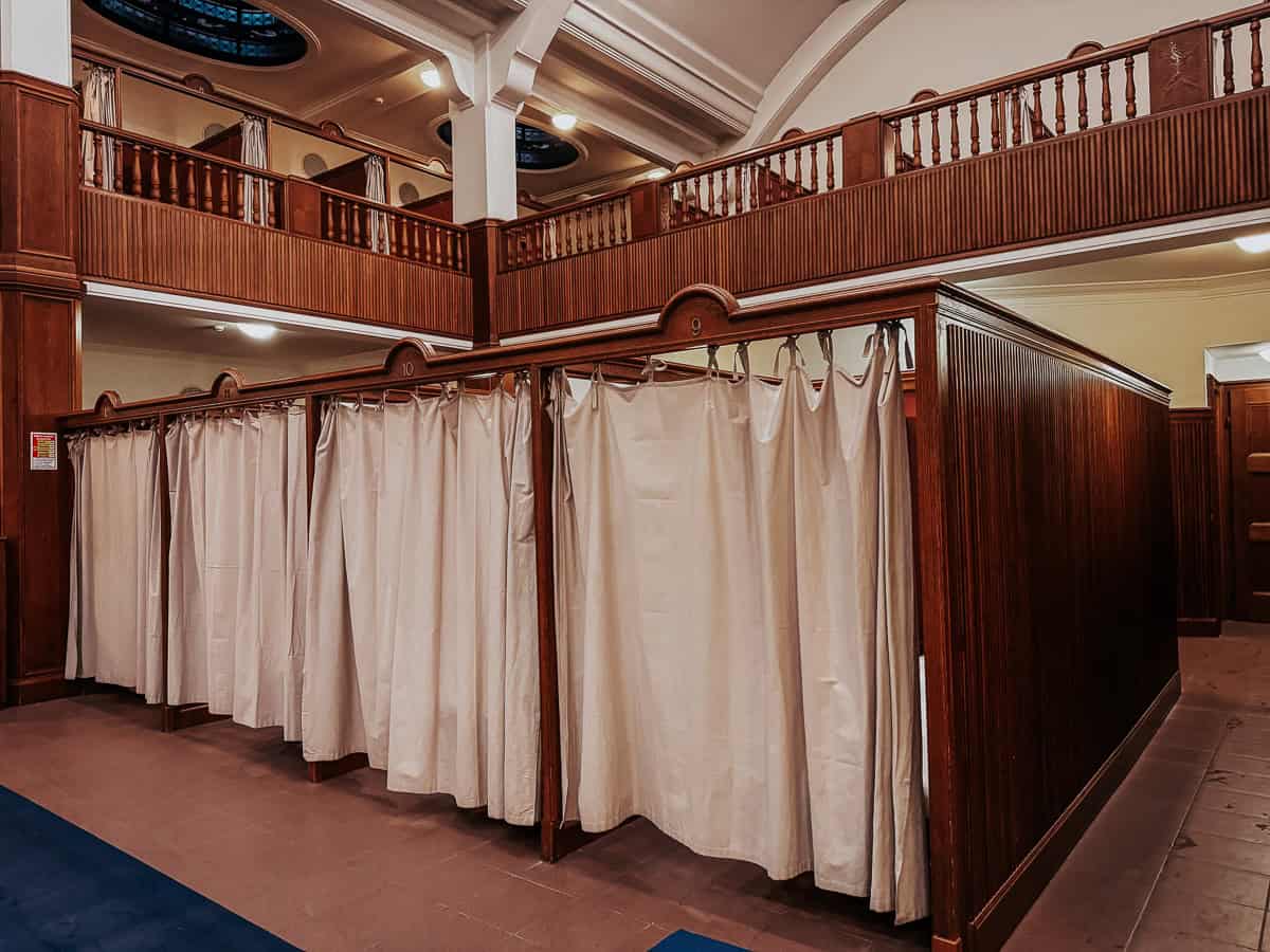 Dressing area in the Gellért Thermal Bath, featuring wooden changing cabins with beige curtains.