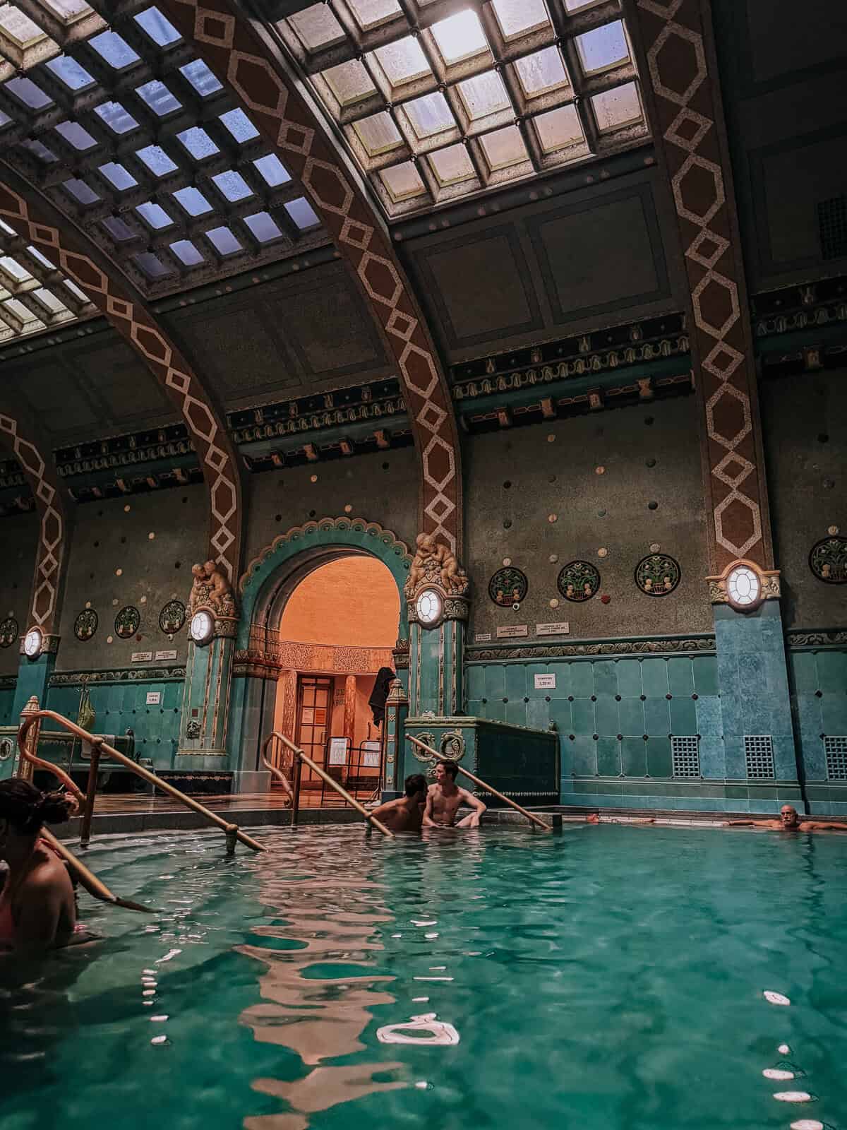 Indoor thermal pool at the Gellért Baths, showcasing ornate arches, a tiled ceiling, and people relaxing in the water.