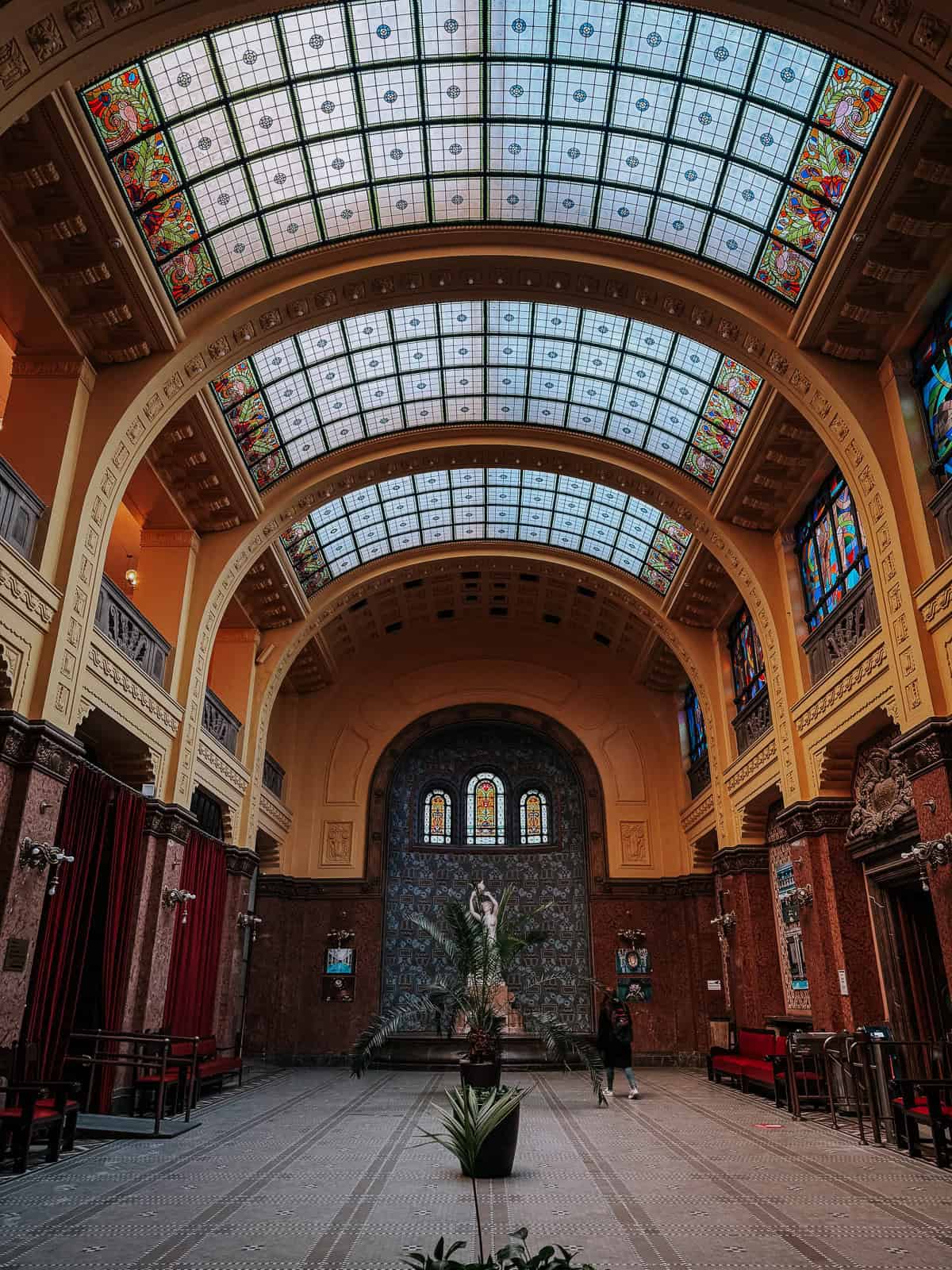 Interior shot of the Gellért Thermal Bath, highlighting the large stained glass ceiling and detailed wall decorations.