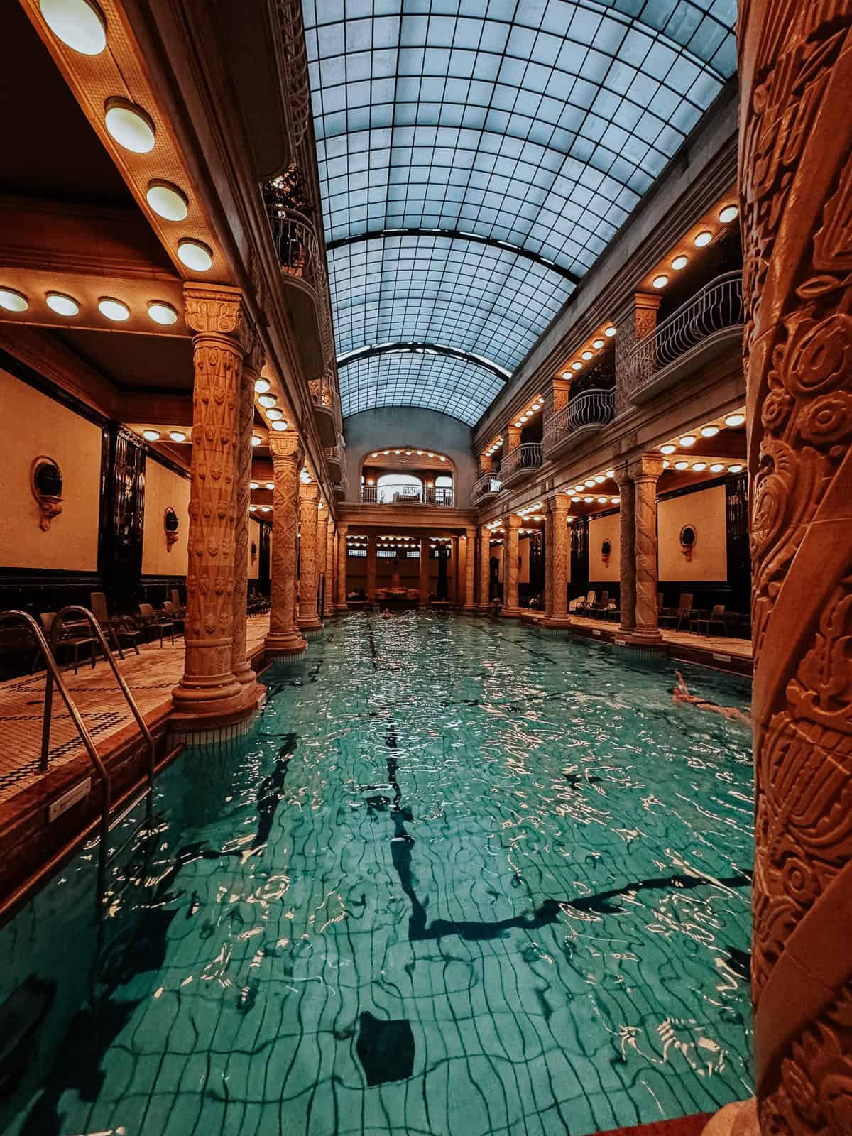 Indoor swimming pool at the Gellért Thermal Bath, featuring a large glass ceiling and ornately decorated pillars.