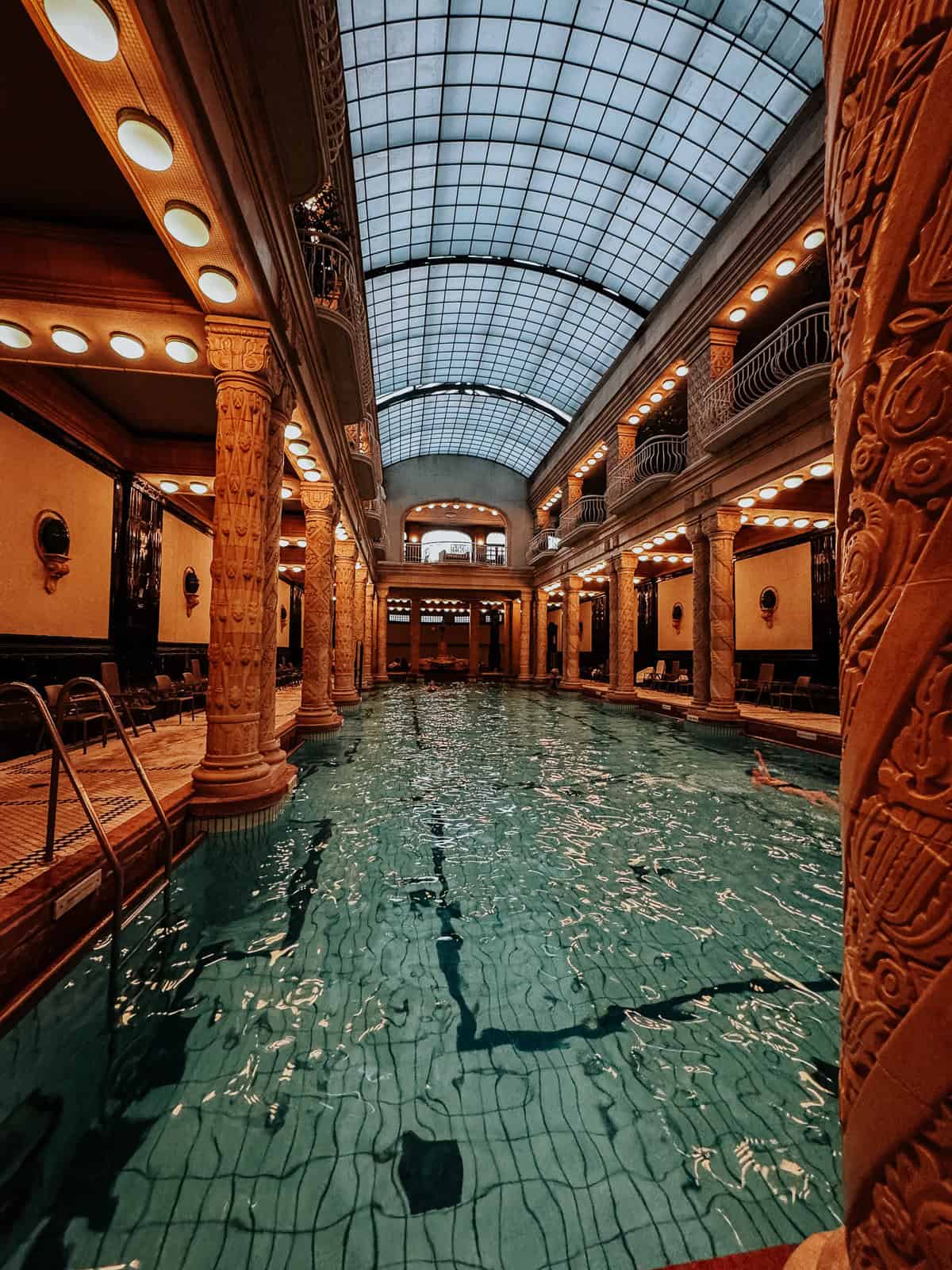 an indoor thermal pool in Gellert baths with blue water and beautiful architecture on the walls