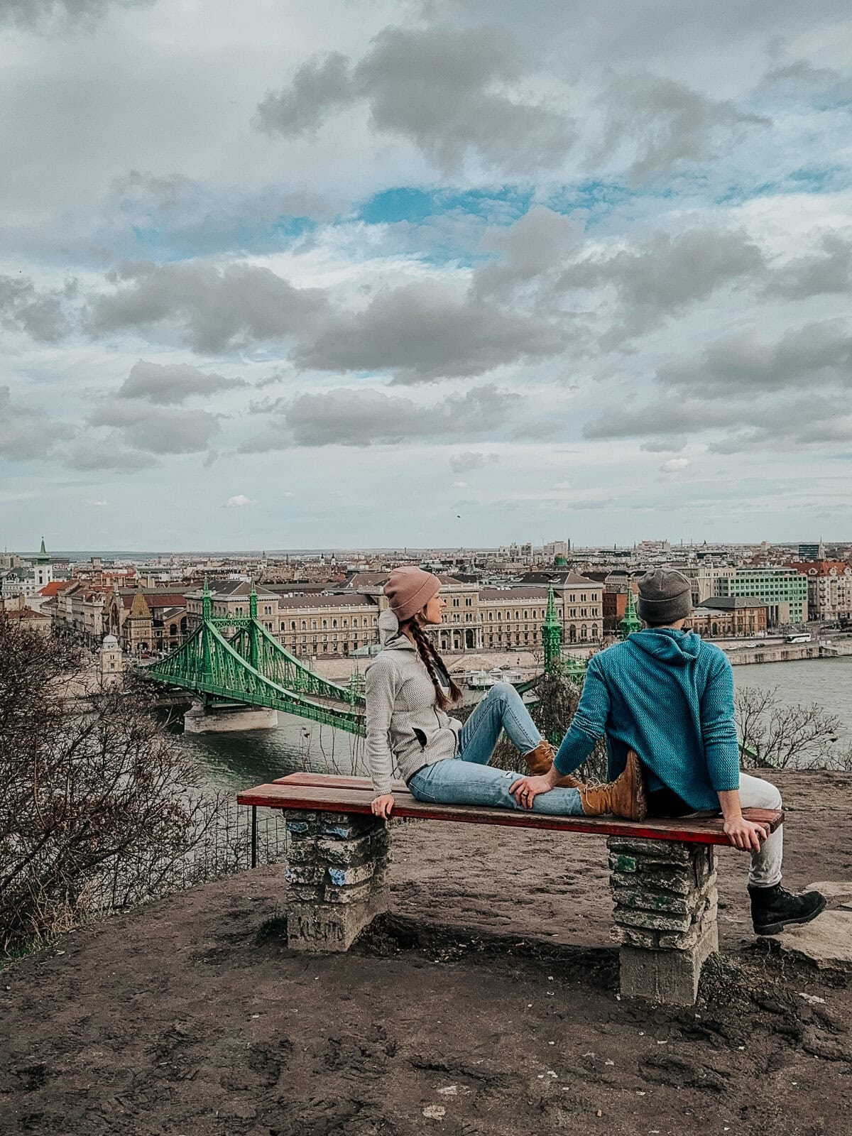 Two people sitting on a bench overlooking Liberty Bridge and the cityscape in Budapest.