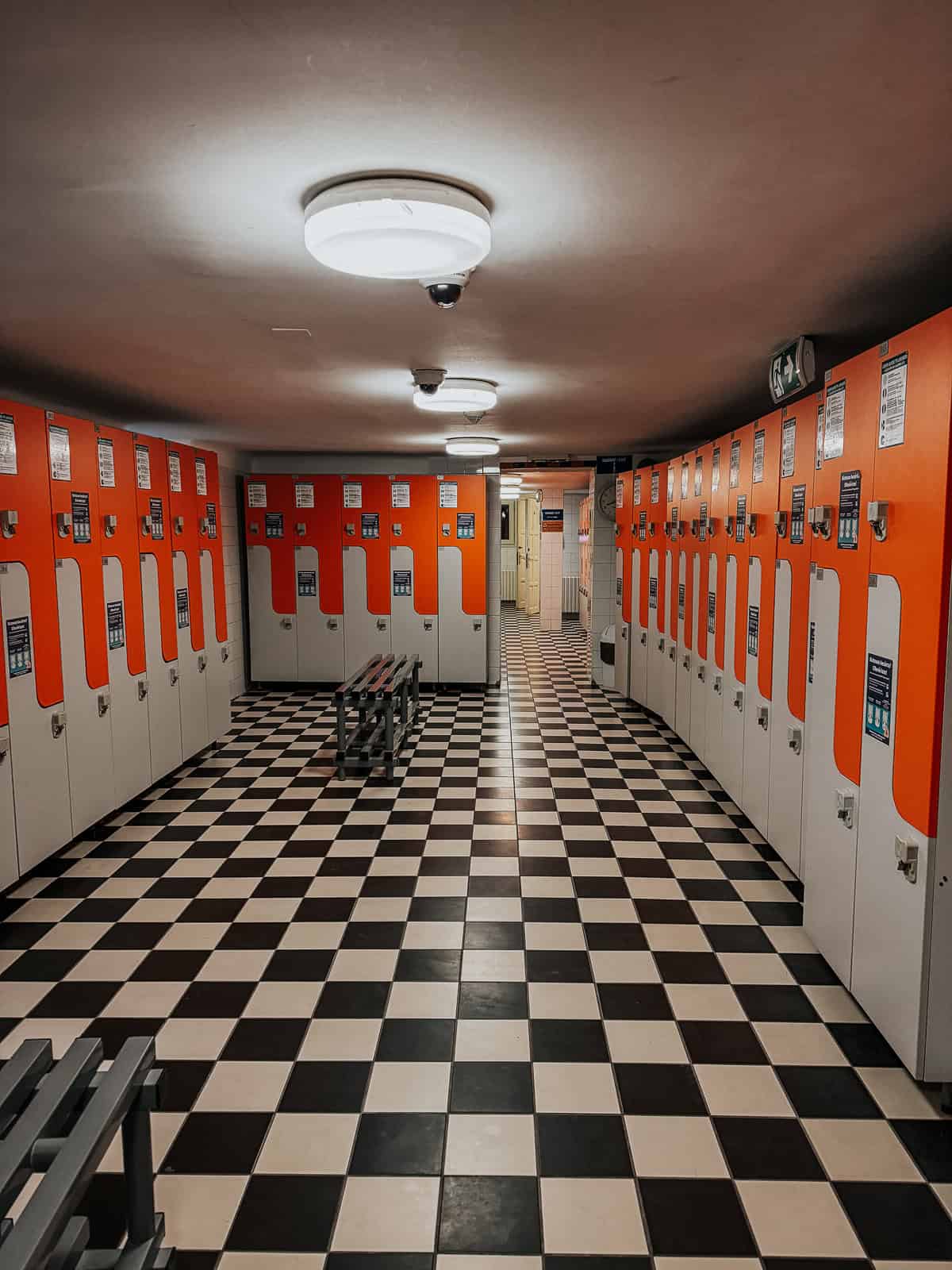 Interior of Lukács Thermal Bath's locker room with orange and white lockers, checkered floor tiles, and benches in the center.