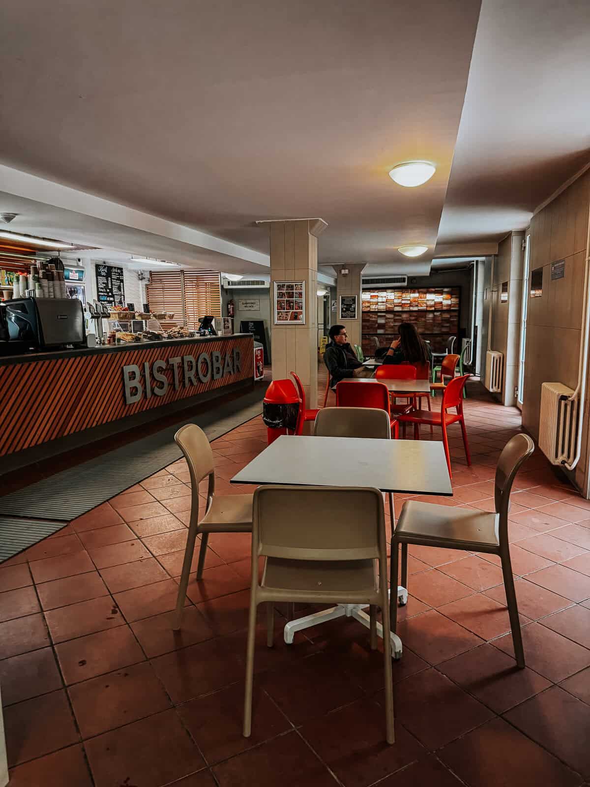 Bistobar inside Lukács Thermal Bath with a modern counter, red and beige chairs, tables, and a relaxed ambiance where patrons are seated and enjoying their time.