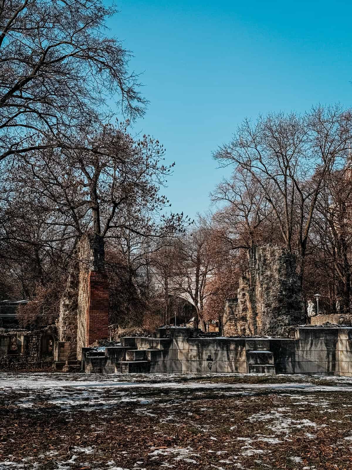 A man sits on ancient stone ruins with a tall, domed tower in the background on Margaret Island.