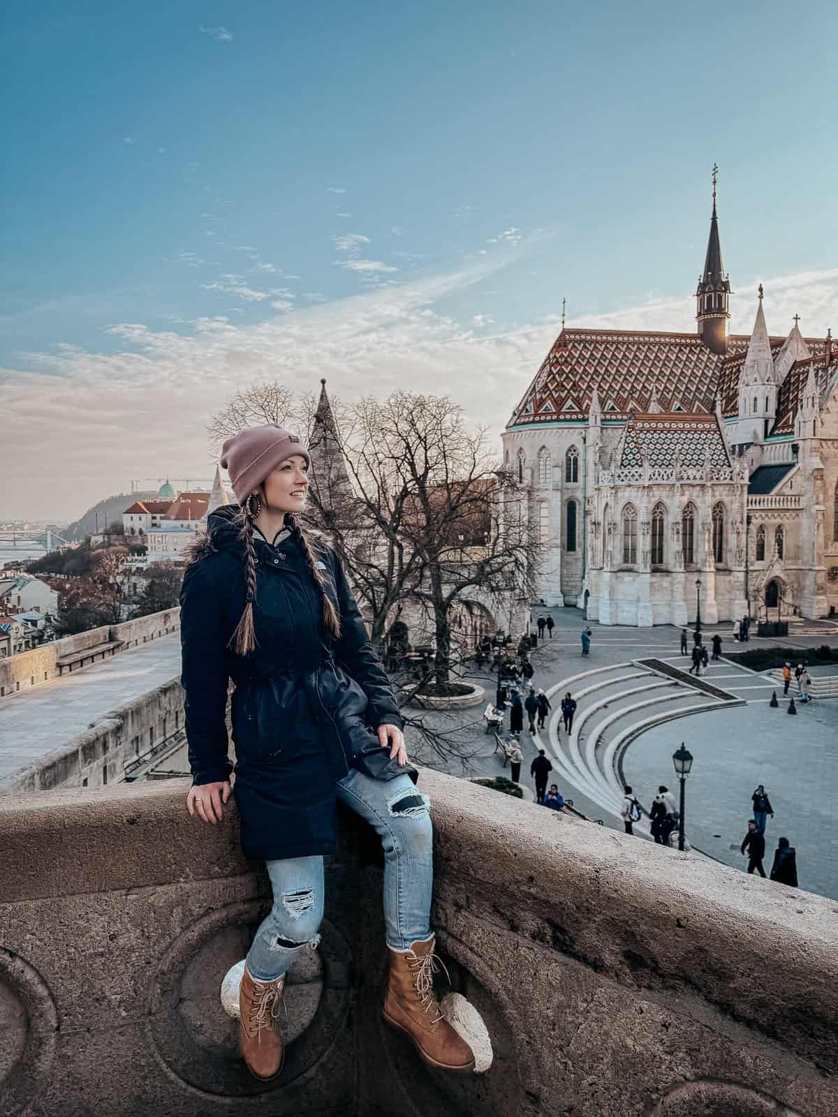 A person sitting on a ledge near Matthias Church, enjoying the view of the historic building and the surrounding area.