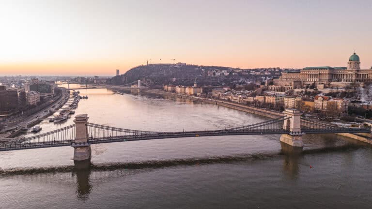 An aerial view of the Chain Bridge and Buda Castle with the Danube River at sunset.