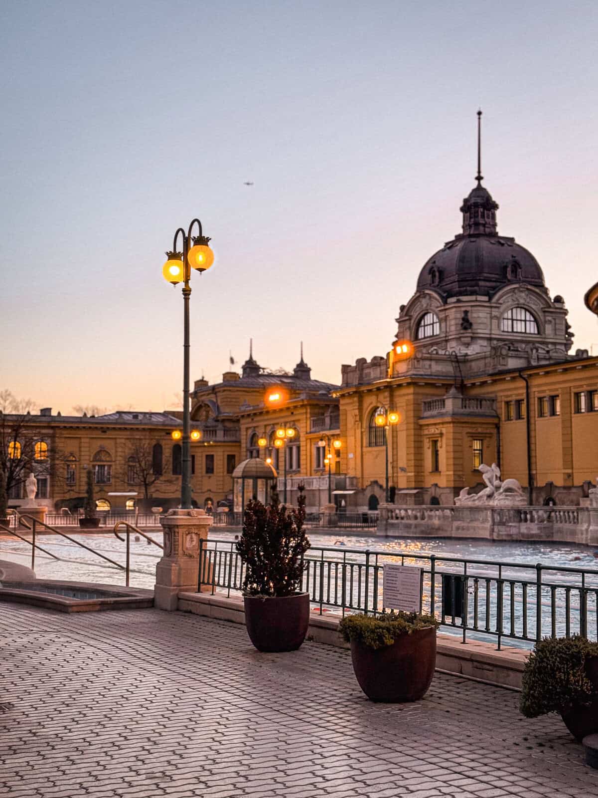 Szechenyi Baths at sunrise with a pink sky and lights coming on