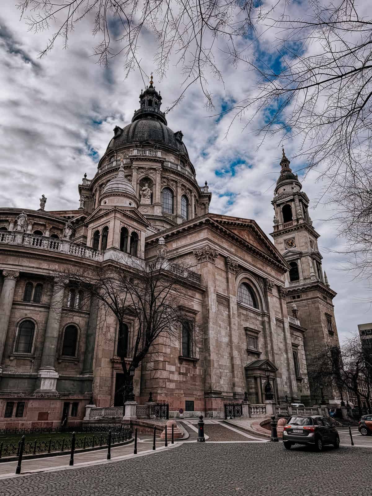 A broader view of St. Stephen's Basilica with its grand dome and tower, surrounded by trees and a partly cloudy sky.