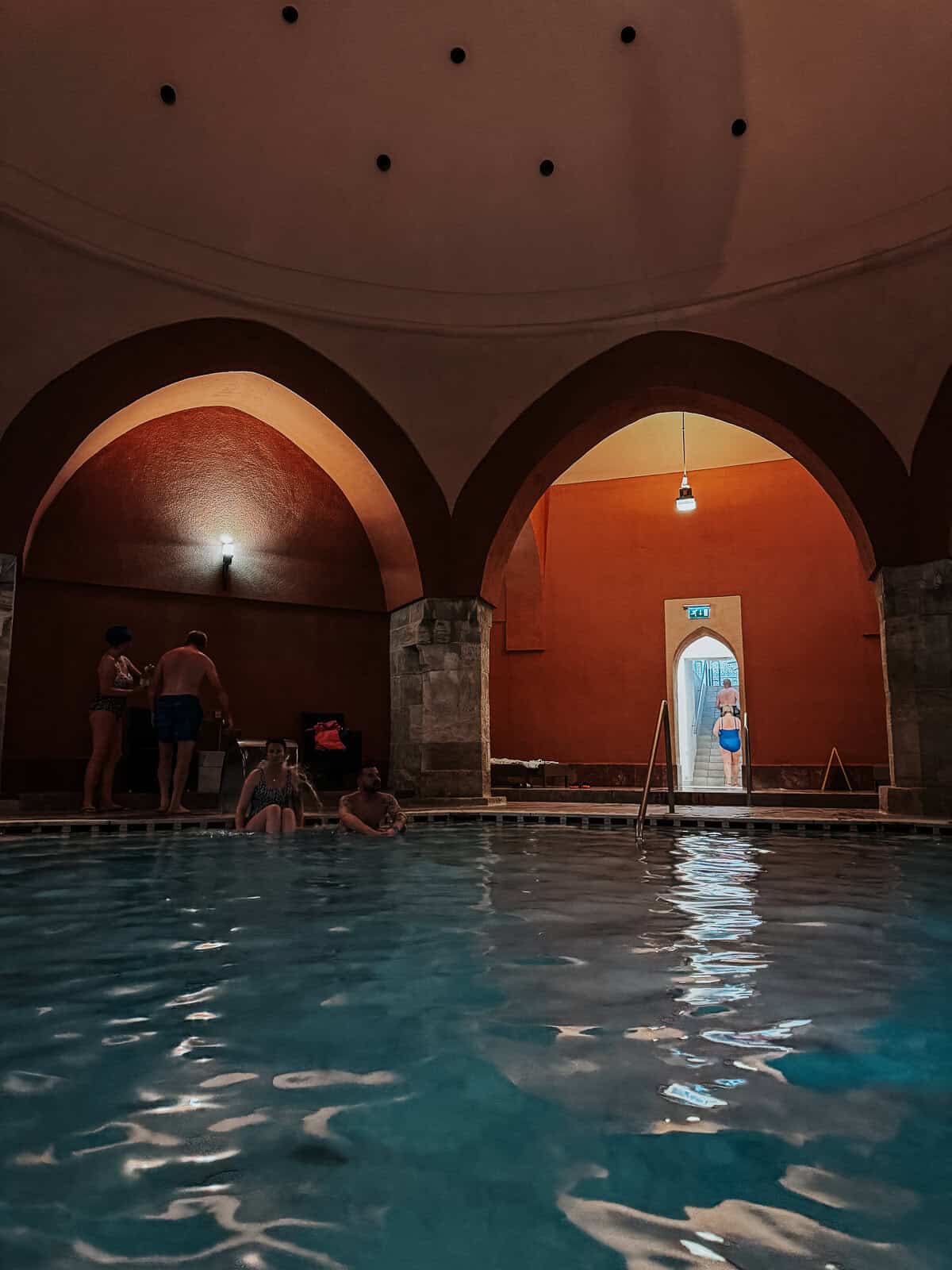 Another view of the indoor pool from a different angle, showing more people in the water and highlighting the architectural details of the arches.