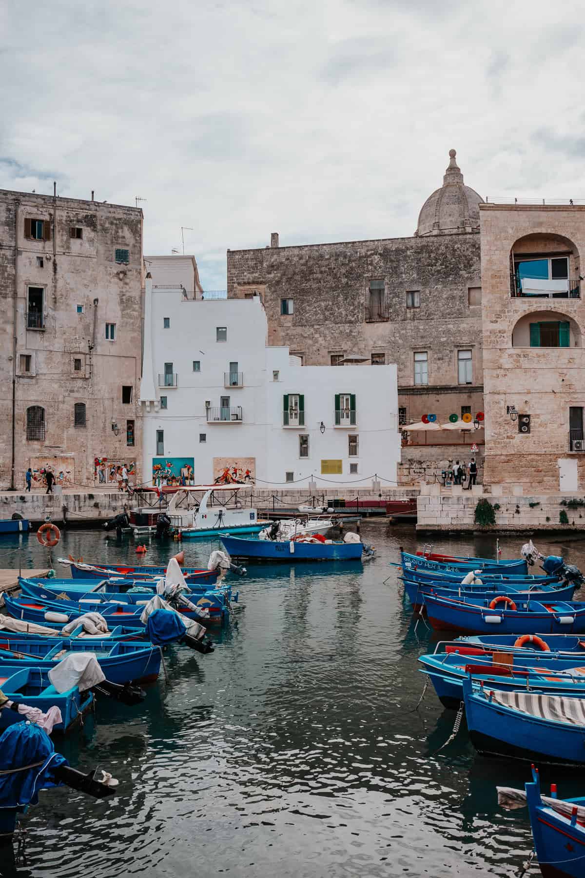 A harbor scene in Monopoli Italy, with traditional blue fishing boats floating in the calm waters, surrounded by historic Mediterranean architecture.