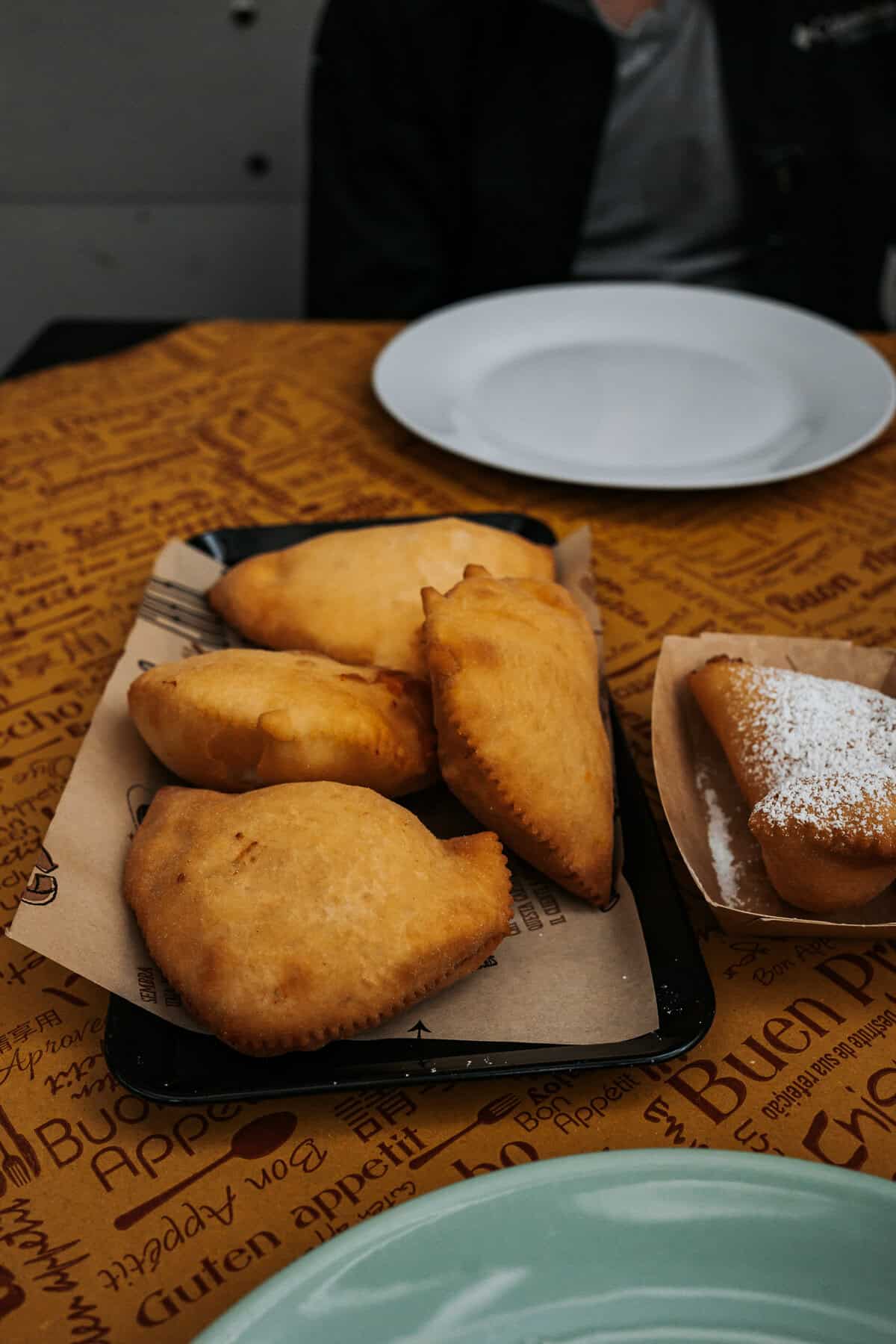 Golden fried panzerotti are served on brown paper with a small sweet pastry dusted in powdered sugar on the side, ready to be enjoyed on a casual dining table.