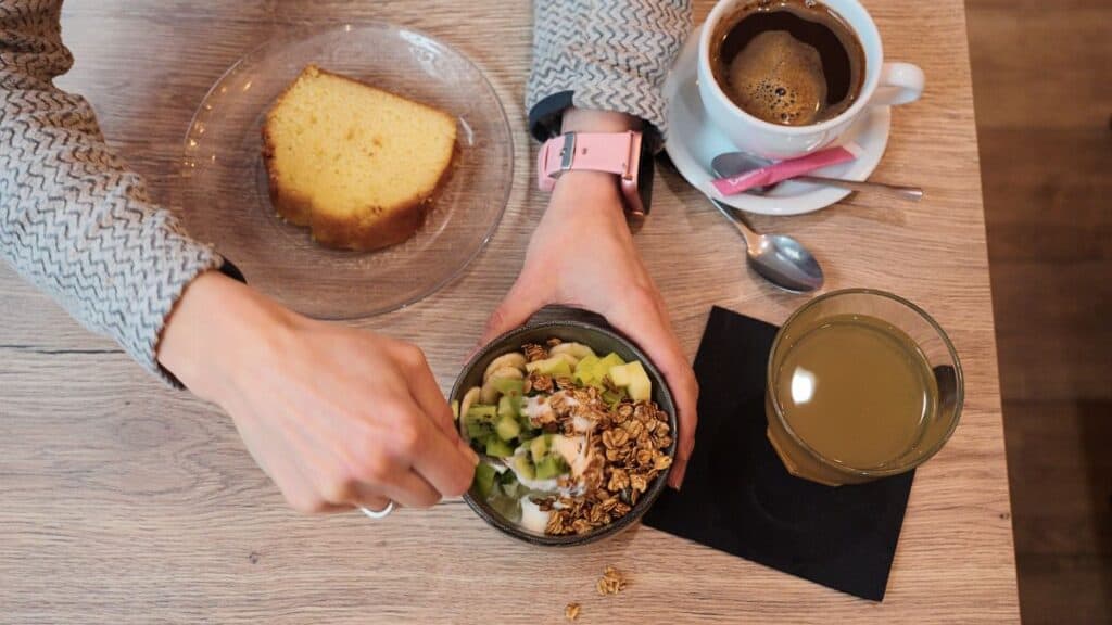 A hand mixing a bowl of fromage blanc with cake and a granola