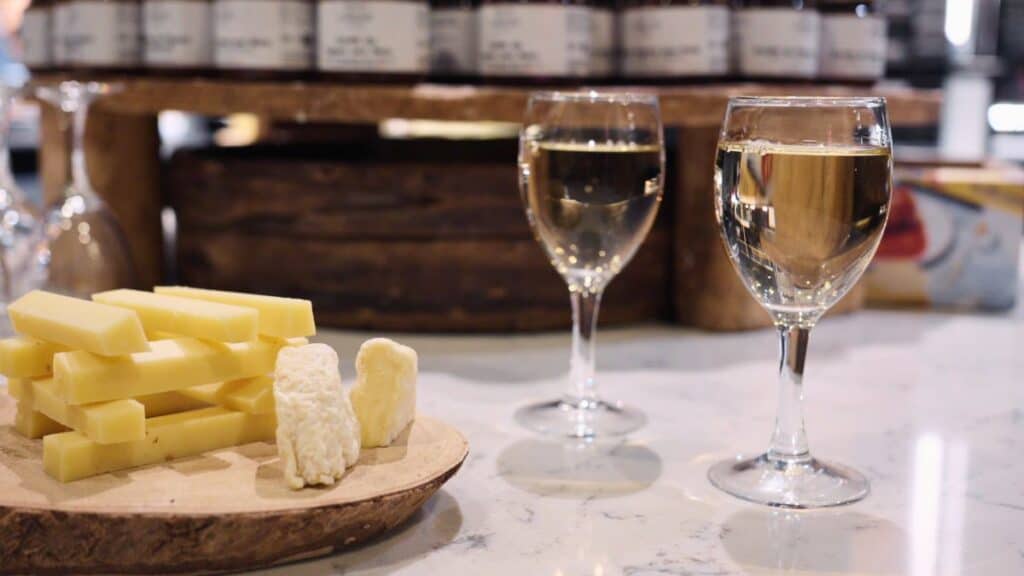 Assorted Lyon cheeses on a wooden board with two glasses of white wine at a French food hall