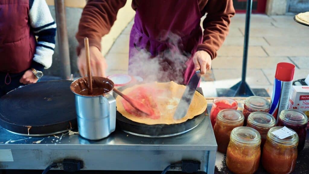 Street vendor cooking a French crêpe filled with pink praline sugar on a hot griddle in Lyon