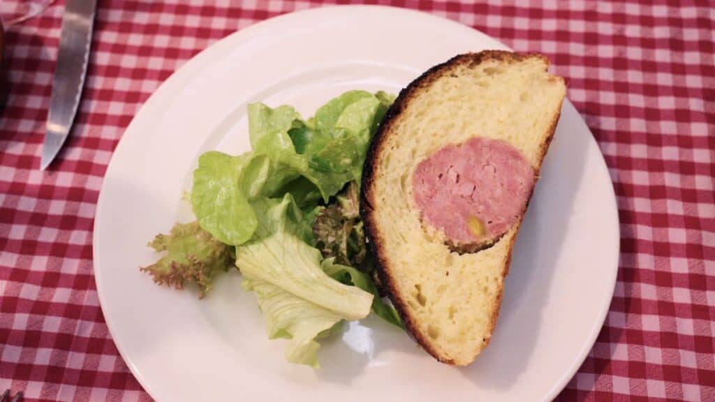Saucisson brioché served warm with salad, showing sausage baked inside brioche bread