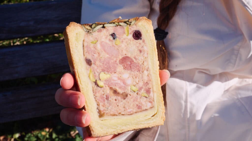 Slice of French pâté en croûte served inside white bread, a classic regional charcuterie snack