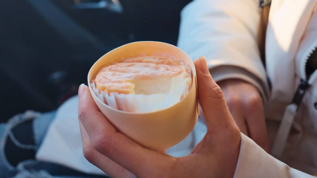 Creamy French soft cheese wrapped in paper and held during a countryside road trip stop