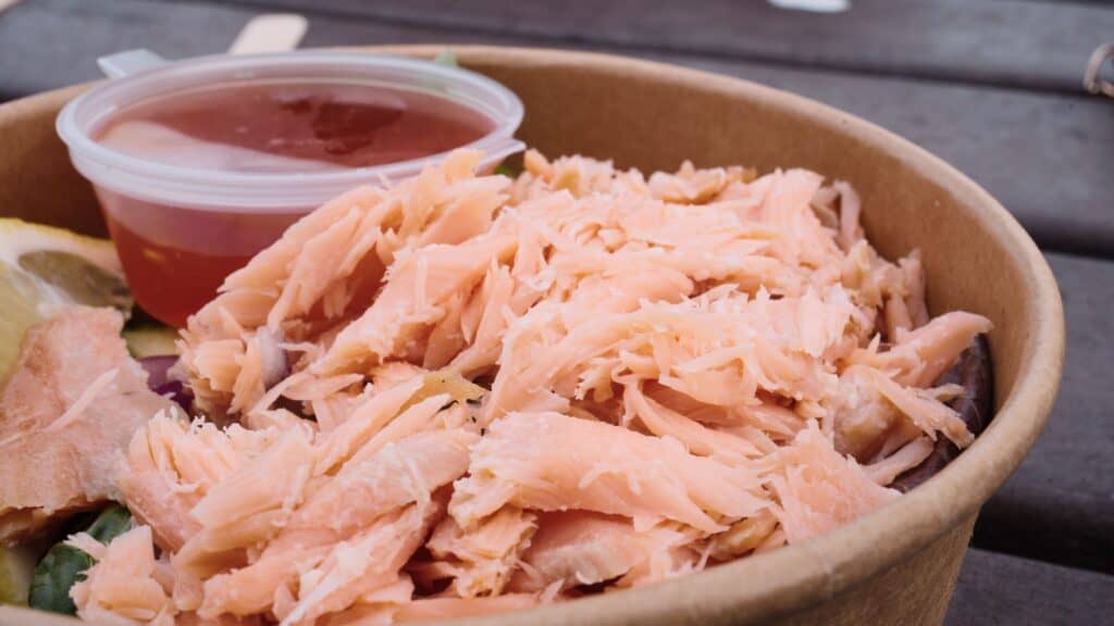 Bowl of shredded salmon served with lemon and a small cup of sauce on a wooden table. The salmon dish highlights fresh seafood commonly featured in traditional Scottish food.