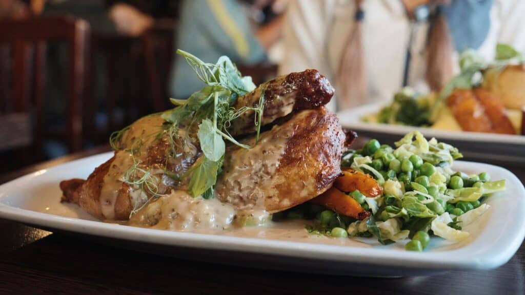 Roast chicken breast covered in creamy herb sauce on a white plate with peas, shredded cabbage, and roasted vegetables. The plated meal represents a comforting traditional Scottish food dish served in a cozy restaurant setting.