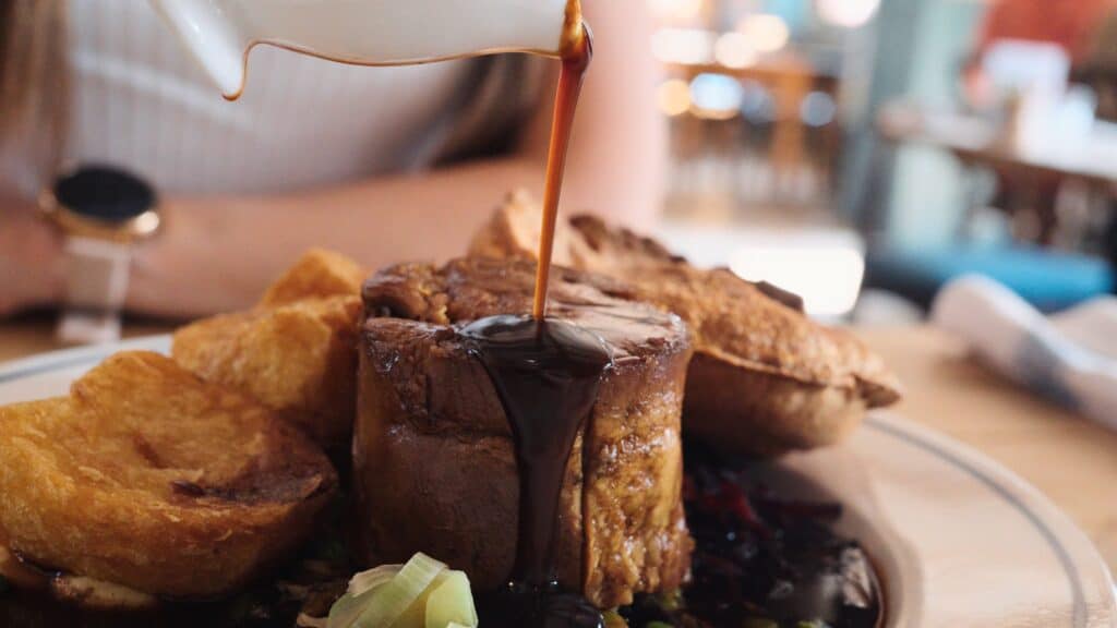 Rich gravy is poured over slices of roast meat served with crispy potatoes and vegetables on a plate. This best restaurants in the Cotswolds dish showcases a hearty and comforting meal.