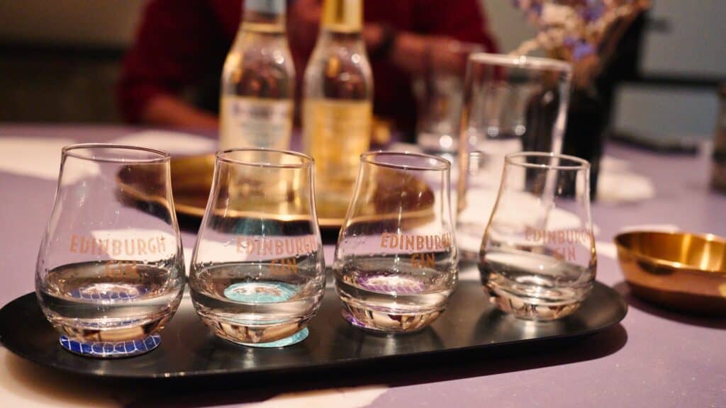 Four tasting glasses on a tray printed with “Edinburgh Gin.” The gin flight represents Scottish craft spirits often enjoyed alongside traditional Scottish food experiences.
