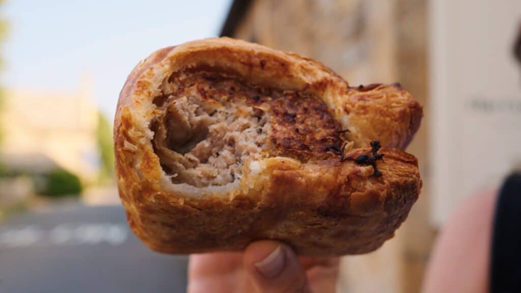 Close up of a hand holding a partially eaten meat pie with a flaky golden crust and savory filling inside. This best restaurants in the Cotswolds food moment highlights a classic British pastry.