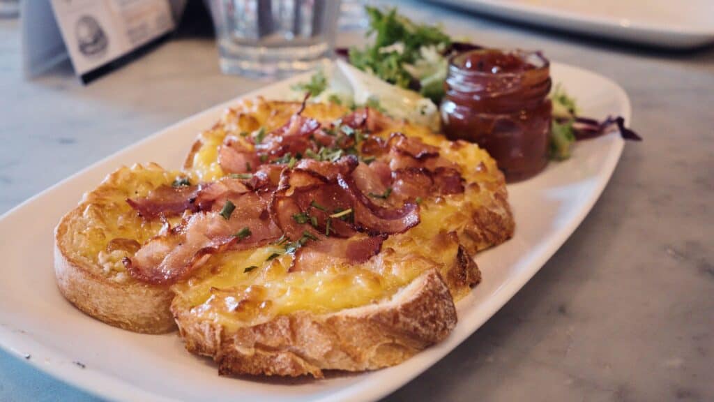 Melted cheese and crispy bacon sit on toasted bread served with a small side of chutney and salad. This best restaurants in the Cotswolds dish presents a comforting café style meal.