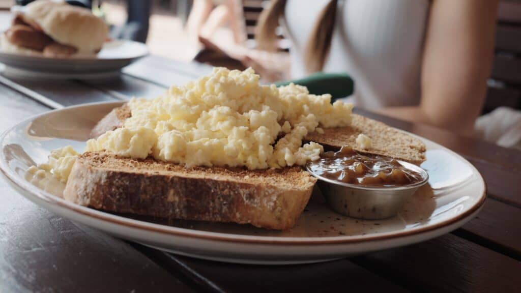 Scrambled eggs piled on toasted bread are served with a side of chutney on a plate at a café table. This best restaurants in the Cotswolds breakfast dish highlights a simple and hearty start to the day.